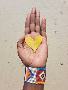 An African woman holding a heart-shaped yellow leaf  on the beach