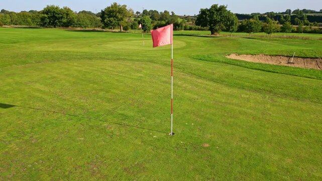 Golf green with red flagstick standing on smooth putting surface, aerial tracking right medium