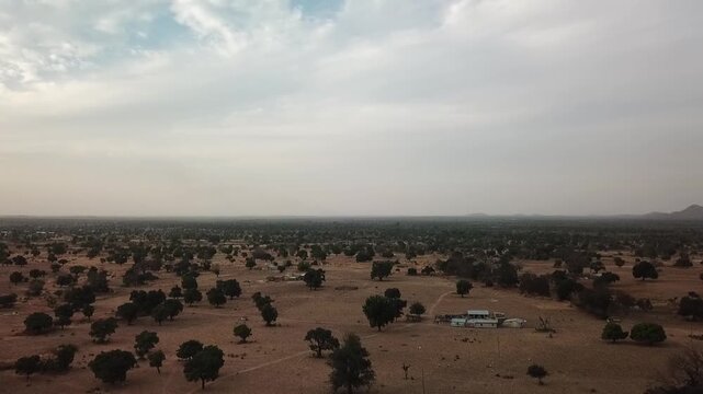 Wide aerial panorama of Northern Ghana's flat savannah landscape dotted with scattered Shea trees and rural settlements under a hazy sky.