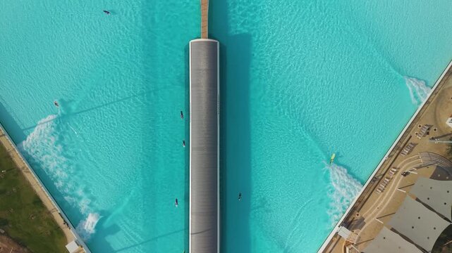 Aerial perspective of surfers at SRF PARK TLV, highlighting the unique fan-shaped pool and clear blue water.