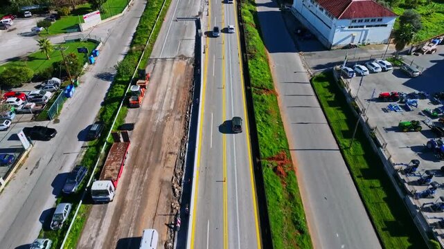 Aerial view of a highway under construction with vehicles, flanked by lush greenery and infrastructure, showcasing the vibrant contrast of nature and transport, Chania, Chania, Greece.