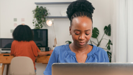 Focused Female Professional in Modern Office Working on Laptop Amid Collaborative Startup Team Environment