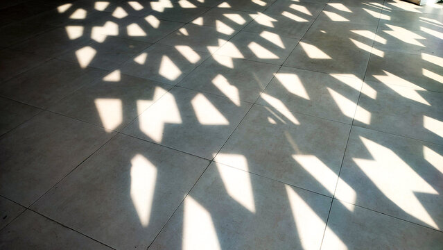 Abstract Islamic background featuring sunlight filtering through a patterned screen, casting geometric shadows on a tiled floor. Minimalist and serene, perfect for Ramadan or Islamic design concepts