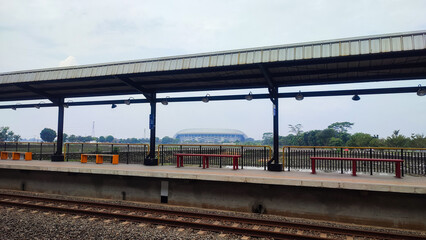 Fototapeta premium Modern train station platform under an overcast sky. A yellow safety line leads toward the horizon, with symmetrical roofing and empty seating creating a quiet, minimal transit and waiting atmosphere.