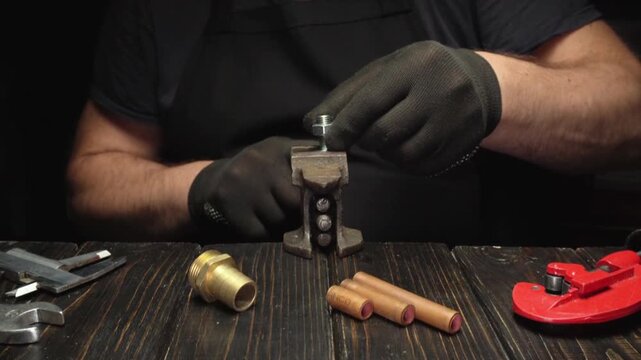 Male technician in black gloves tightens a metal bolt using a vice grip on a wooden workbench surrounded by various tools and materials