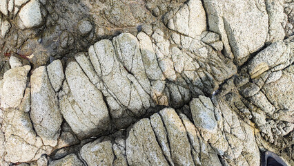 High-angle close-up of rugged grey coastal rock formations shaped by volcanic activity and ocean erosion, showcasing cracked, bulbous textures and natural stone patterns along the shoreline.