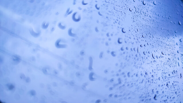 Close-up of raindrops clinging to a glass window with a soft, blurred view of a road and greenery in the background, creating a calm, moody rainy-day atmosphere