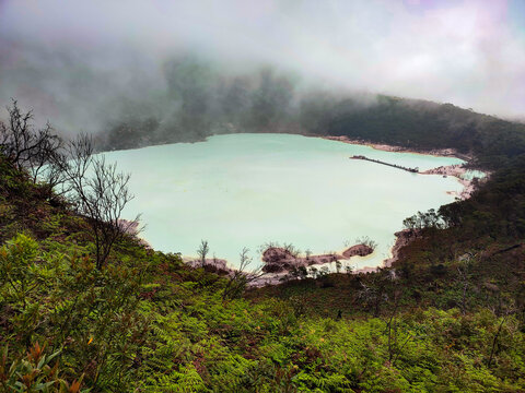 Aerial view of Kawah Putih&rsquo;s turquoise and milky-white crater lake located at Mount Patuha in West Java, surrounded by volcanic cliffs, dead trees, and mist. Adventure, nature, travel concept