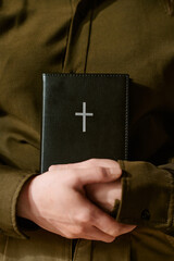 Caucasian young adult woman holding closed black Bible with silver cross on cover, hands gently...