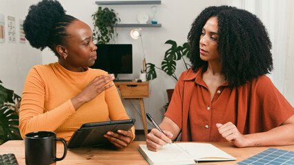 Two Women Collaborating At A Home Office Desk With Notebook And Tablet In A Cozy Studio