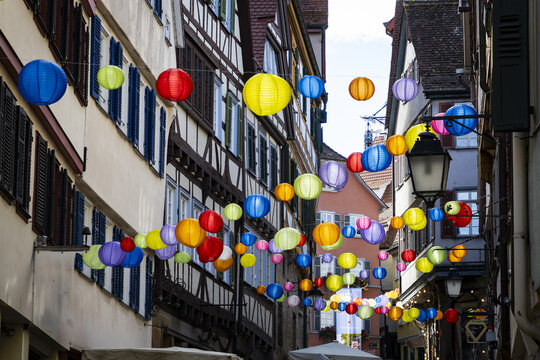View of vibrant lanterns strung across a narrow street framed by half-timbered buildings, casting colorful glows in Tubingen, Baden-Wurttemberg, Germany.
