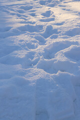 Deep snow at sunset. The meadow is covered with white snow. Footprints in the snow, snowdrifts. Winter landscape. Winter snow background, side view with selective focus