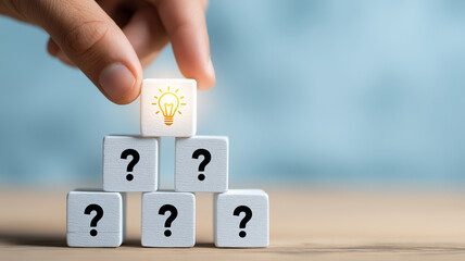 Hand putting cubes with question mark symbol icons stacked on wooden table with light bulb symbol on top, faq, question and answer or support concept
