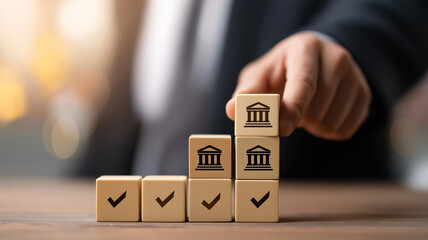 Businessman hand putting wood block with bank building icon on top of wooden cube marked with checkmarks