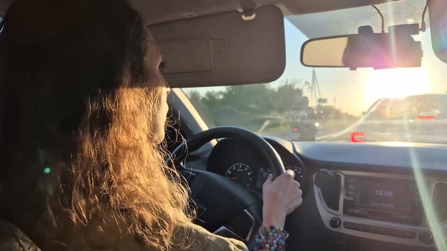 Driving, woman, sunset: long-haired female driver travels down a highway road during golden hour trip adventure.