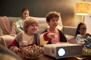 Group of Caucasian and Asian children and teenagers watching movie together at home, sitting on...