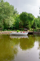 Fototapeta premium Rain in the summer park. A pond with a boat under raindrops.