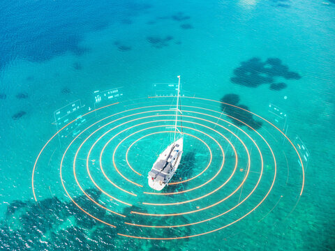 An aerial view of a white sailboat on clear turquoise water, with a digital interface overlay featuring concentric orange circles and various navigational data panels.
