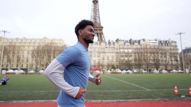 Determined african american athlete enjoying his daily cardio workout, jogging on a stadium running track with the iconic eiffel tower visible in the beautiful parisian background