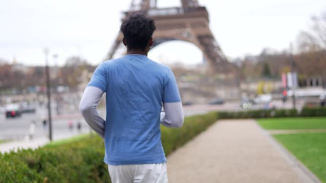 Athletic young african american man jogging in a public park with the famous eiffel tower in the background, representing a healthy and active lifestyle in the beautiful city of paris, france