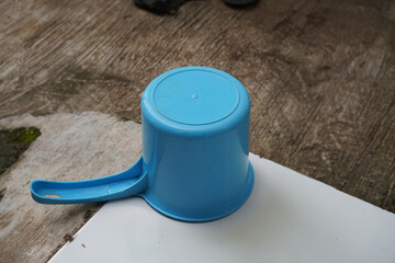 Blue plastic water dipper placed on a white tiled ledge. Everyday household utensil, water use, and simple home setting concept.