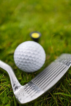 Golf ball and iron club on wet green grass.