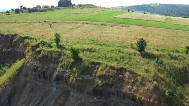 Aerial view of a layered rock formation with sparse vegetation clinging to its steep surfaces, showcasing natures raw beauty, Racos, Judetul Brasov, Romania.