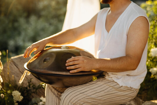 Man playing a handpan drum outdoors at golden hour, creating a calm and atmospheric moment surrounded by nature and warm sunlight.