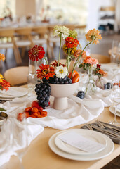Fototapeta premium Elegant wedding table centerpiece with seasonal flowers, grapes, and fruit arranged on a natural linen table.