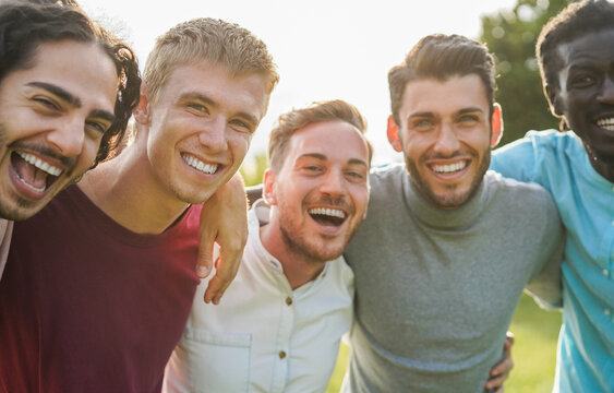 Happy male friends having fun together outdoor - Group of multiracial men hugging each other at city park - Friendship and lifestyle concept - Main focus on blond man face