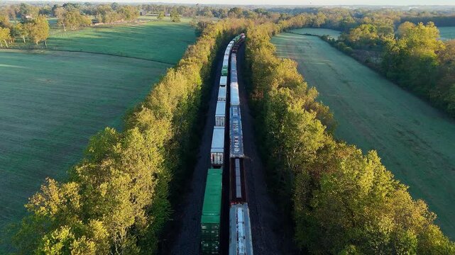 Long freight train moving through rural landscape, aerial view of transport logistics