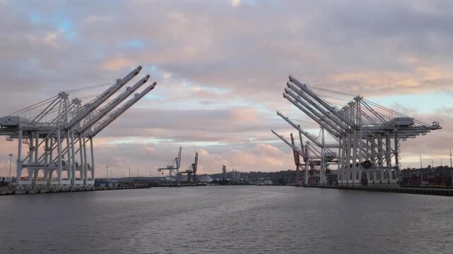 Gimbal wide panning shot of industrial cranes as seen from a moving boat on Elliott Bay during sunset at the Port of Seattle, Washington. 4K at 30 FPS