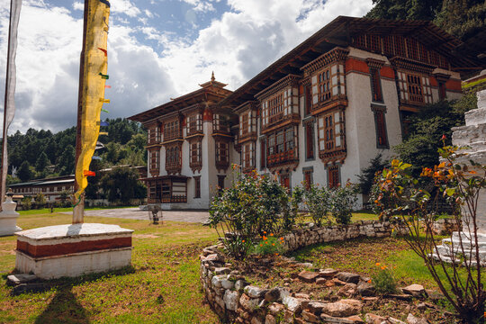 View of a majestic building with intricate woodwork and vibrant prayer flags fluttering in the breeze, standing proudly in a lush green landscape, Jakar, Bhutan.