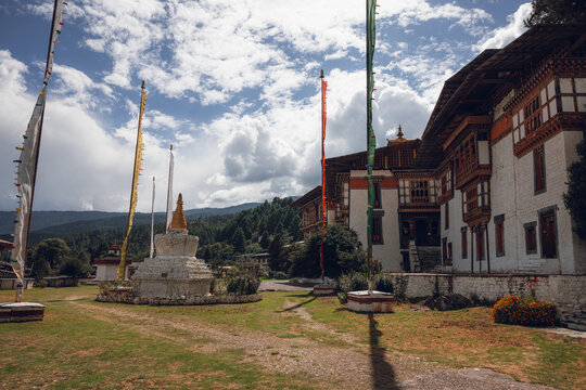 View of prayer flags fluttering beside ancient stupas and traditional architecture under a cloudy sky, Kurjey Lhakhang, Jakar, Bumthang, Bhutan.