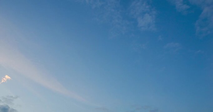 Timelapse of clear blue sky with some wispy cirrus clouds and smaller cumulus clouds. Serene, open atmosphere, with color gradient suggesting either early morning or late evening light. 4K footage.