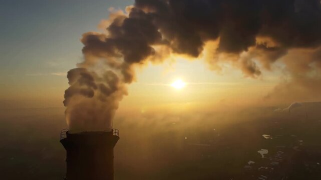 4K cinematic aerial video tall industrial smokestack emitting thick, dark smoke hazy sky during golden hour sunset. Volumetric sunlight beams filter smoke dust particles dramatic lighting. scale smoke