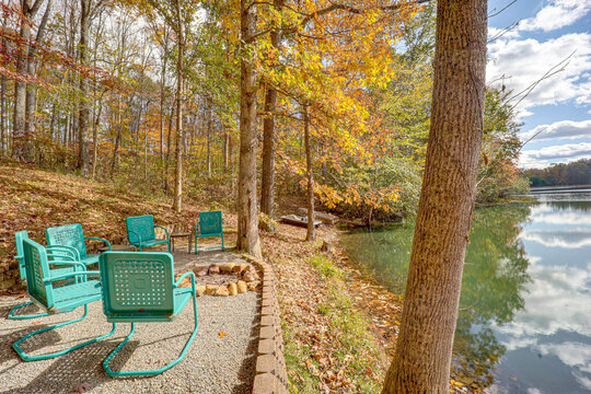 View of teal chairs circle a rustic firepit, nestled between vibrant autumn foliage and tranquil lake waters in Hamden, Ohio, United States.