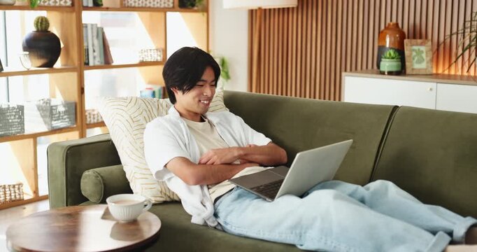 Relax, happy man and laugh with laptop on couch, funny movie and watch comedy series for entertainment. Online streaming, comic film or asian person in home to rest, subscription platform or computer
