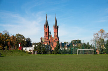 Obraz premium Playing field, football goal. Church of Holy Family (kościół Świętej Rodziny) in background, brick Neo-Gothic two-towered temple was built between 1904 and 1906. Tarnów, Poland.