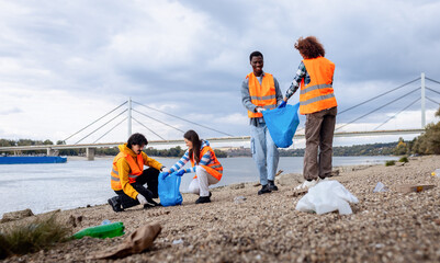 Smiling volunteers collecting garbage in blue bags during river cleanup.
