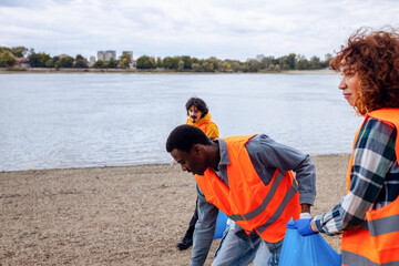 Smiling volunteers collecting garbage in blue bags during river cleanup.