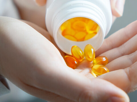 Close-up of golden fish oil capsules pouring from white bottle into woman palm for health