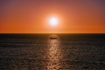 Obraz premium Red Sunset over ocean horizon with a boat in sunlight