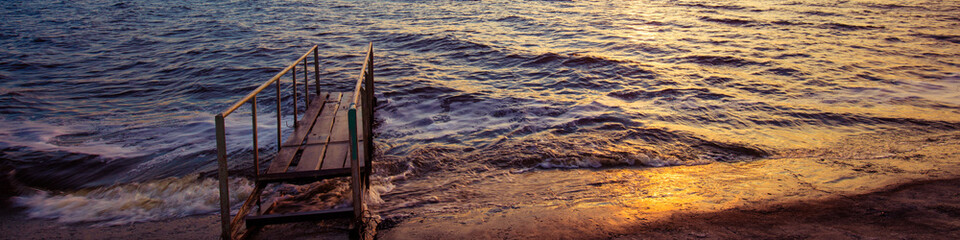 Evening on the beach, sunset over sea, pier on the sea