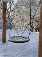 A children's swing covered in snow in a park. European winter, snowfall, natural disasters.