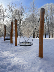 A rope swing covered in snow in a park. European winter, snowfall, natural disasters.