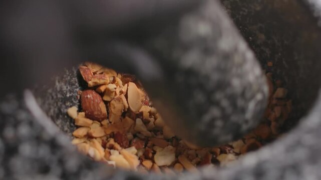 A hand grinds a mixture of nuts in a granite mortar. For a pie made with filo pastry