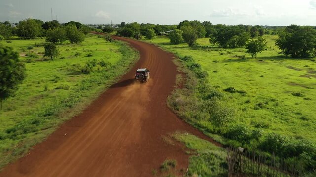 Aerial view of a dirt road cutting through lush green fields, showcasing the contrast between the red earth and verdant landscape, Daboya, Savannah Region, Ghana.