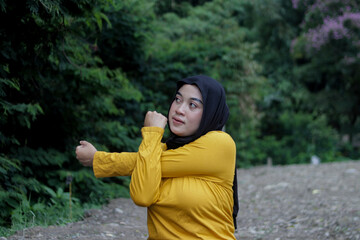 Young Asian woman wearing a black hijab and yellow shirt practices yoga exercises outdoors. Mindfulness, wellness, and healthy lifestyle concept.