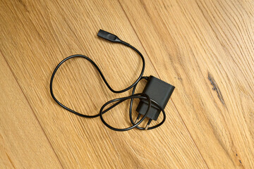 A charger is placed on a wooden table. The black cable is neatly laid out beside it.